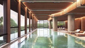 A modern indoor swimming pool with clear glass walls, wooden beams, and lounge chairs.