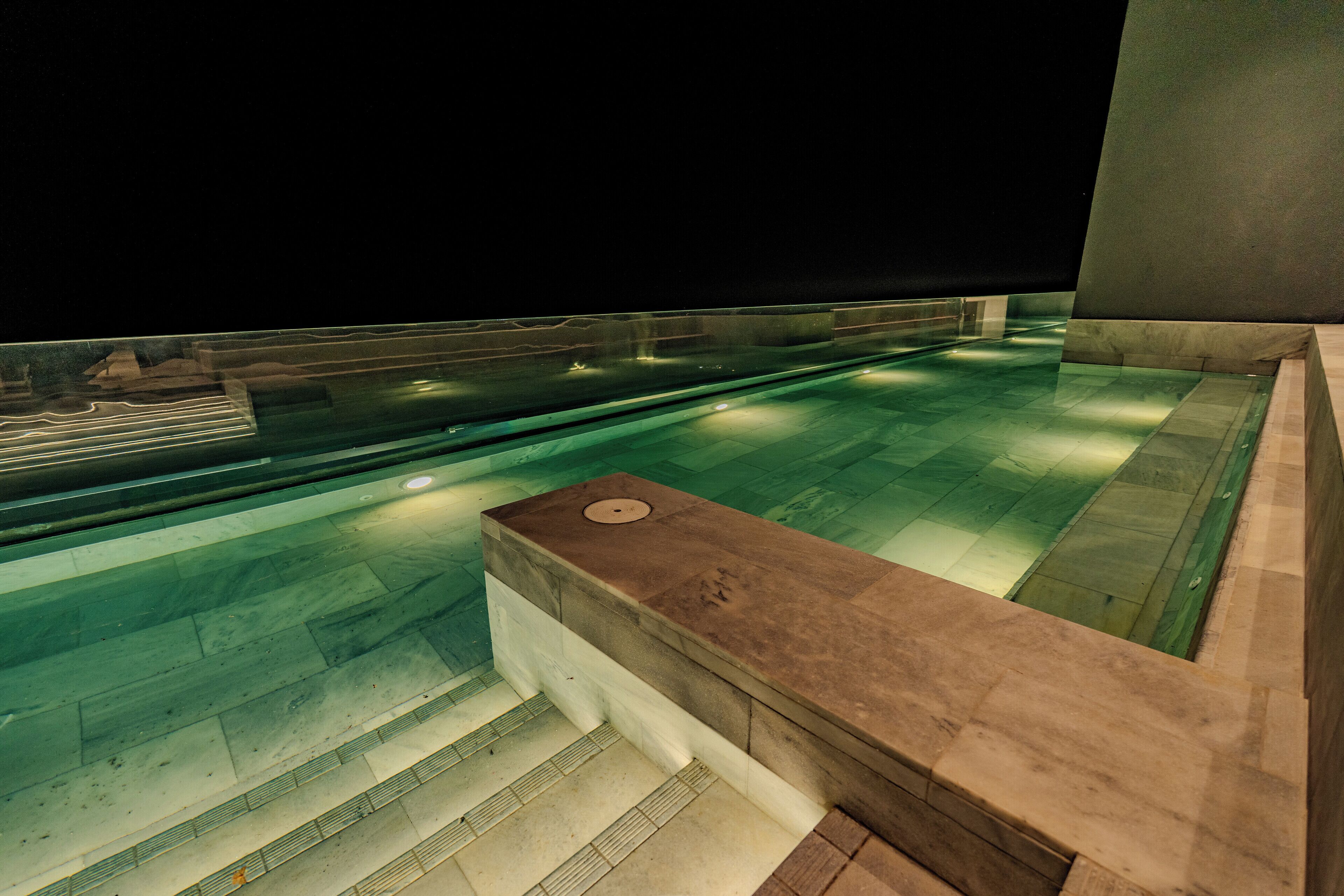Piscina interior moderna con agua cristalina, un borde de piedra y fondo oscuro.