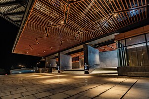 An outdoor area with a modern architectural design, featuring a geometric ceiling structure and a well-lit entrance with a staircase.