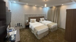 A hotel room with two beds, a desk with a chair, a TV, and a minibar. - Mayar Golden Hotel (Madinah)