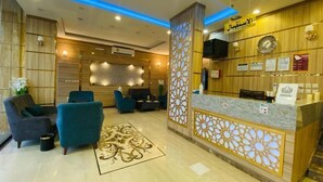 A hotel reception area with a wooden reception desk, blue chairs, and a decorative wall panel. - Mayar Golden Hotel (Madinah)