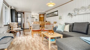 Un salon chaleureux avec un canapé gris, des chaises en bois, une table basse en bois et un coin repas comprenant une table et des chaises en bois.
