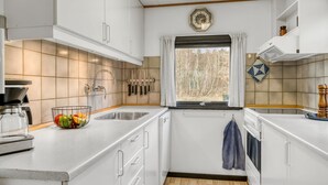 Une cuisine moderne avec des meubles blancs, une grande fenêtre et une vue sur les arbres à l’extérieur.