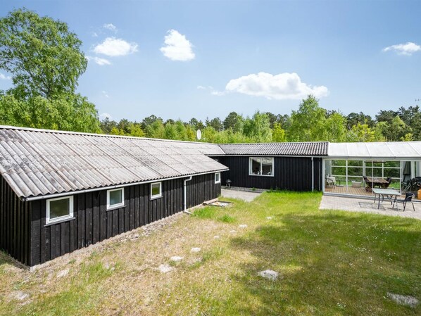 Un bâtiment moderne de couleur noire, doté d’un toit en métal, d’un patio vitré aménagé avec du mobilier d’extérieur et d’une cour verdoyante.