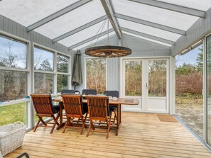 Une terrasse couverte avec une table et des chaises, de grandes fenêtres et un luminaire suspendu.