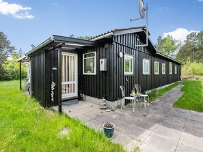 Une maison en bois noire, dotée d’un patio, d’une antenne parabolique et d’un petit jardin.