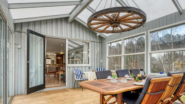 Une terrasse en bois avec une table et des chaises, de grandes fenêtres et un ventilateur de plafond.