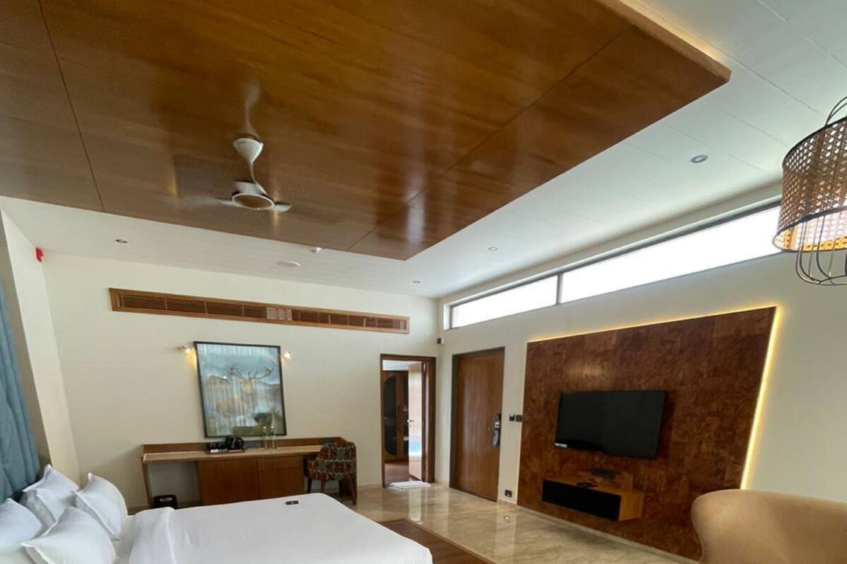 Une chambre d’hôtel spacieuse, dotée d’un grand lit, d’un bureau, d’un téléviseur fixé au mur et d’un coin salon avec deux fauteuils et une table basse.