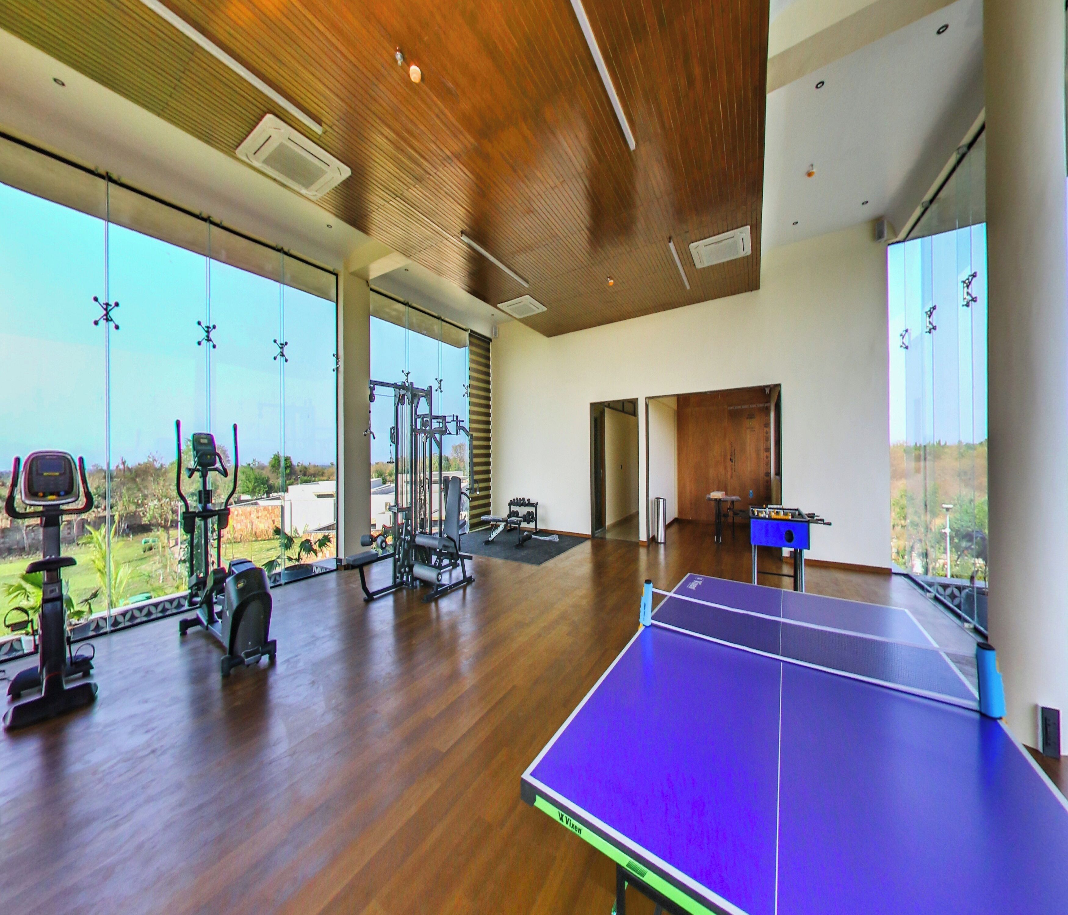 A spacious indoor area with a ping pong table, exercise equipment, and large windows offering a view of the outdoors.