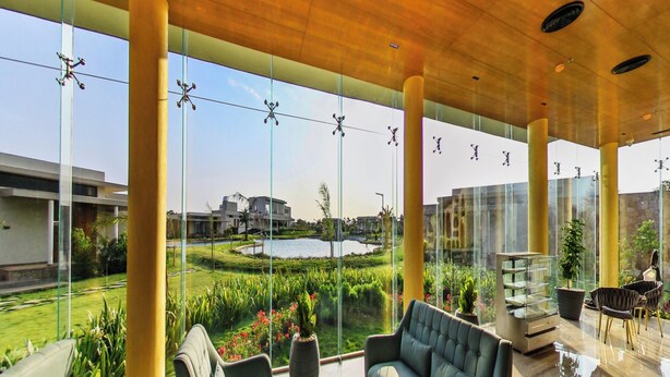 Un espace de détente extérieur moderne, doté de murs en verre, de sièges confortables et offrant une vue sur un jardin aménagé et un bâtiment.