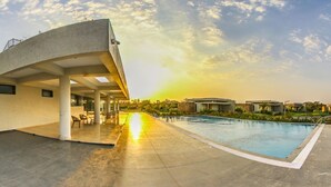 Un espace piscine moderne, doté d’une structure de bâtiment aux lignes courbes, de coins salon extérieurs et offrant une vue dégagée sur le coucher de soleil.
