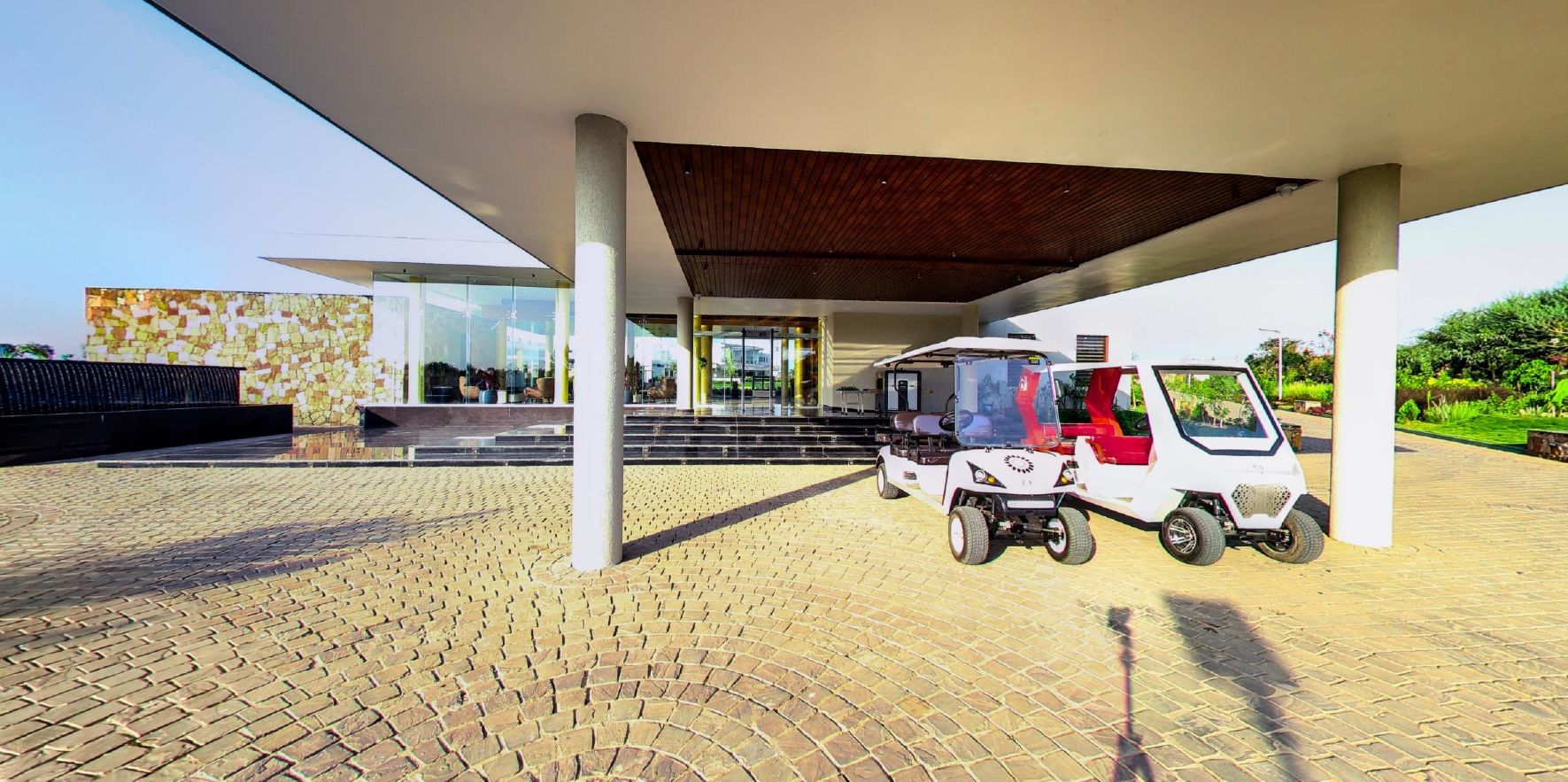 Un espace extérieur abrité avec un chemin pavé, un véhicule blanc et, au fond, un bâtiment au design moderne.