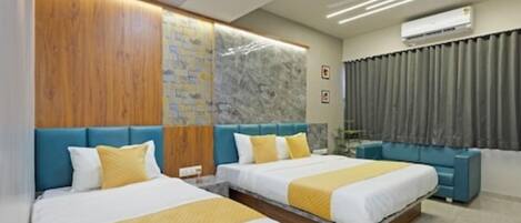 A hotel room with two beds, a blue sofa, a marble wall, and an air conditioning unit.