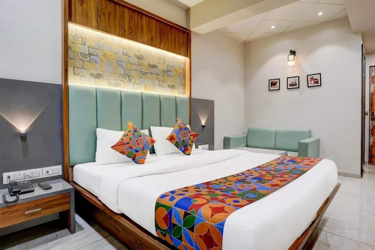 A modern hotel room with a large bed, a wooden headboard, a bedside table with a phone, and a wall-mounted light.