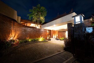 Un espacio exterior bien iluminado con un camino pavimentado, muros de piedra y una palmera.