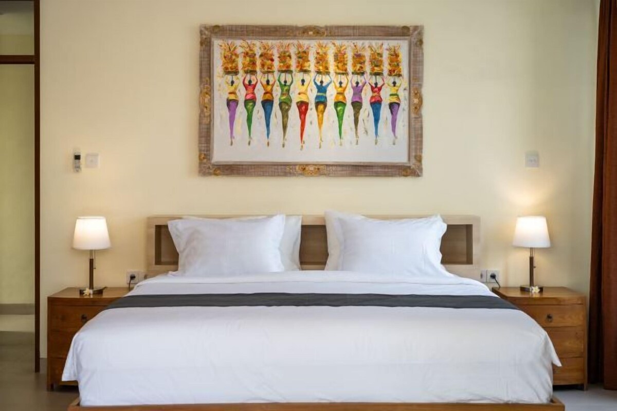 A hotel room with a large bed, two bedside tables with lamps, and a framed artwork on the wall.