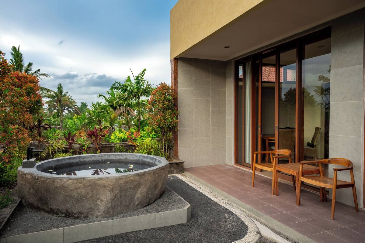 Un área de estar al aire libre y moderna con una fuente de agua de concreto, rodeada de exuberante vegetación tropical.