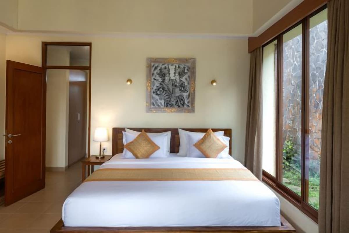 A hotel room with a large bed, a painting on the wall, and a view of the outdoors through a window.