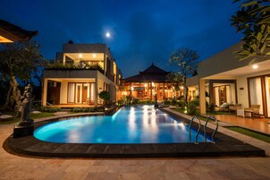 Un hotel moderno con piscina, mobiliario exterior y un edificio tradicional al fondo.