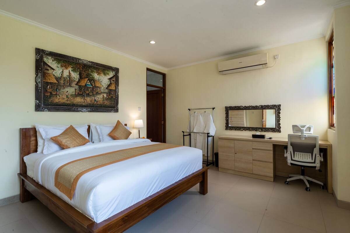 Un dormitorio con una cama grande, un escritorio, una silla, un espejo y un cuadro en la pared.