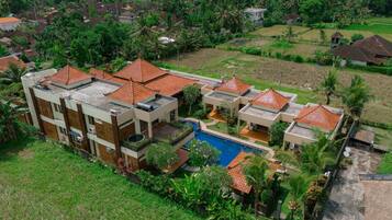 Una zona residencial con casas modernas, techos de tejas rojas, una piscina central y abundante vegetación.