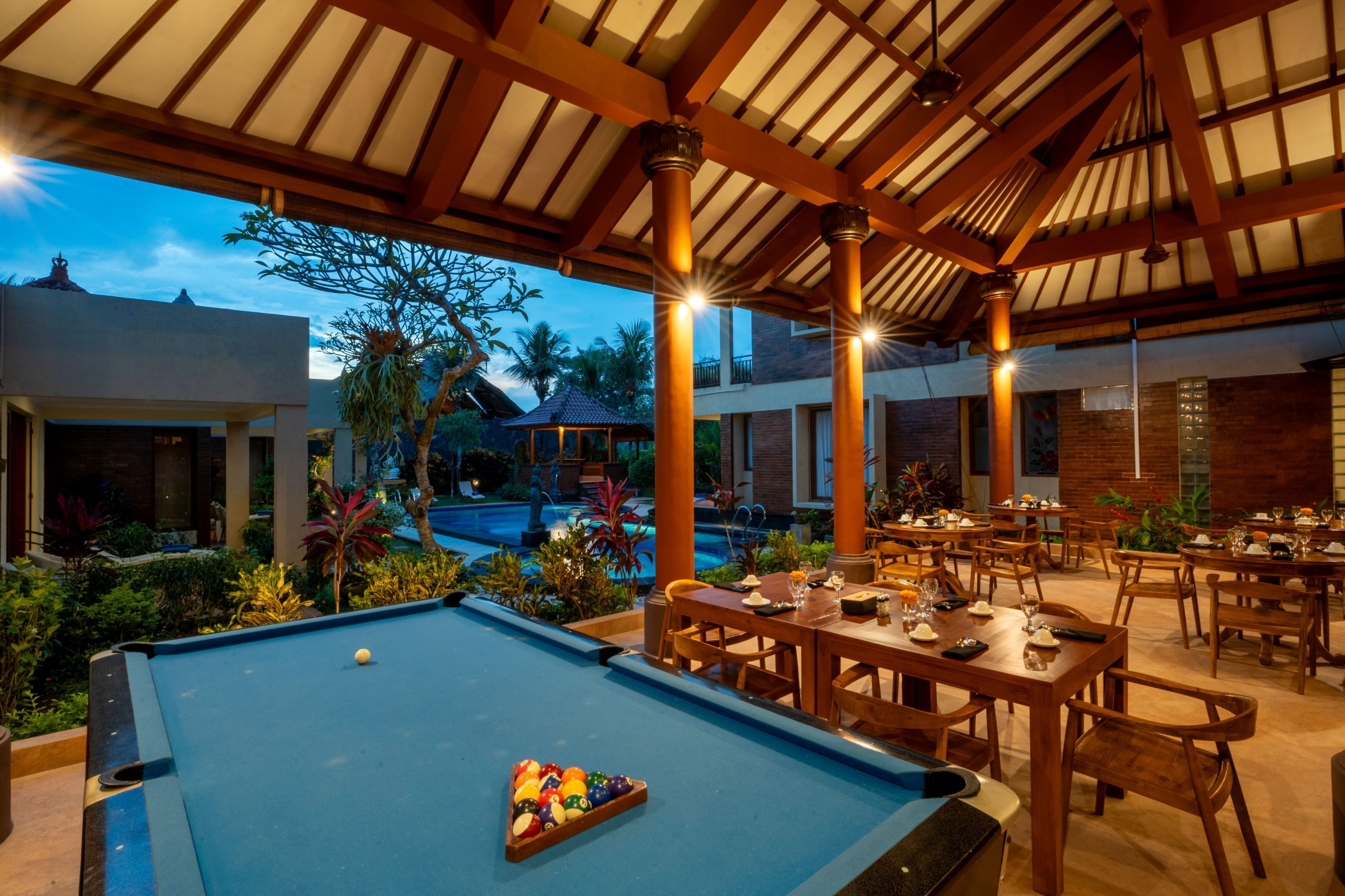 Un espace extérieur avec une piscine, une table de billard, des tables et des chaises pour prendre les repas.