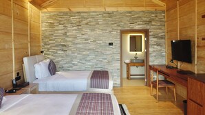 A wooden cabin bedroom with two beds, a desk, a TV, and a bathroom with a stone wall. - Gangtey Pinewood Resort (Wangdue Phodrang)