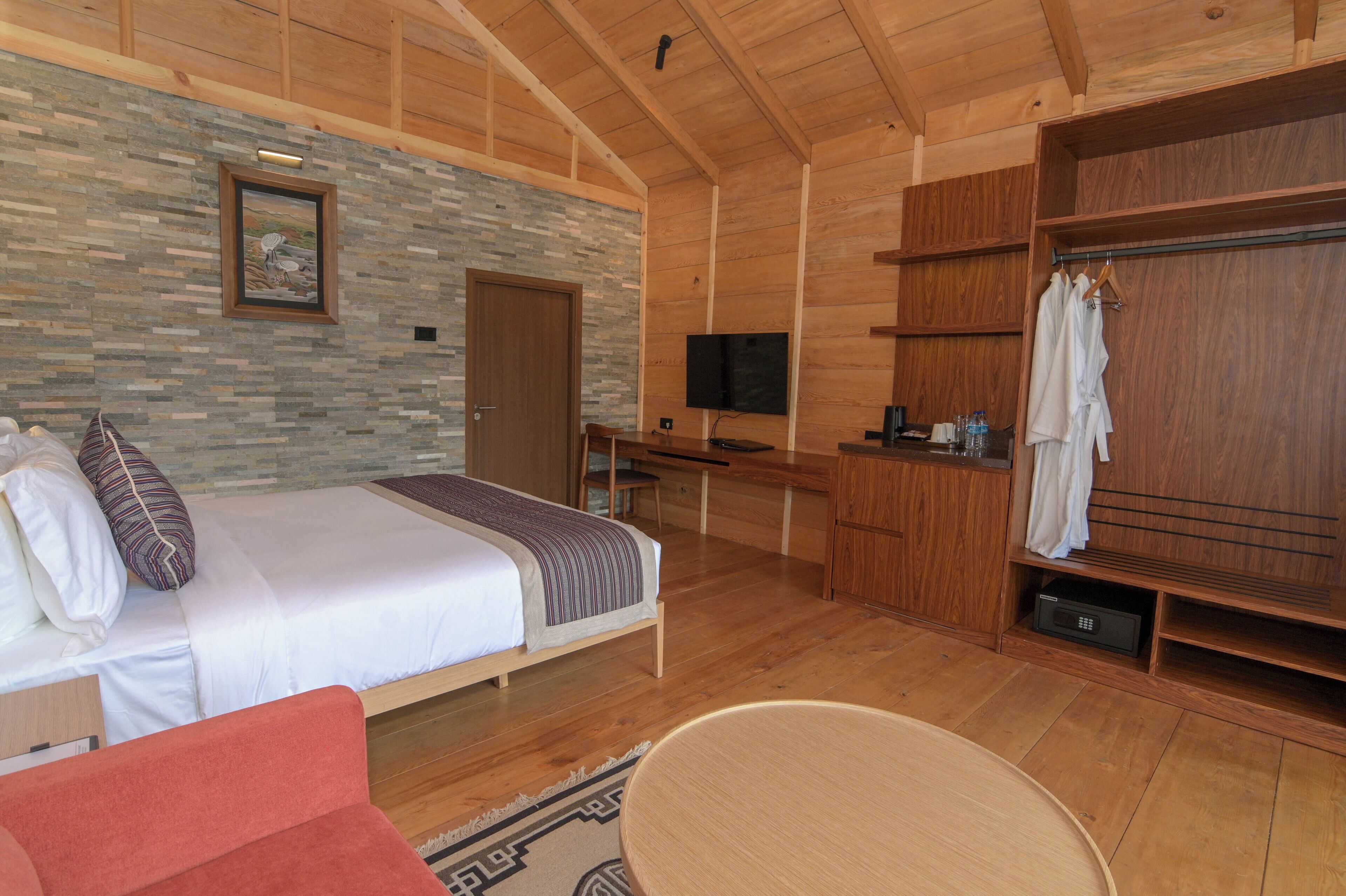 A wooden cabin room with a bed, a desk, a TV, and a wardrobe.