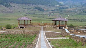 A rural landscape with two wooden gazebos and a paved path leading to them. - Gangtey Pinewood Resort (Wangdue Phodrang)