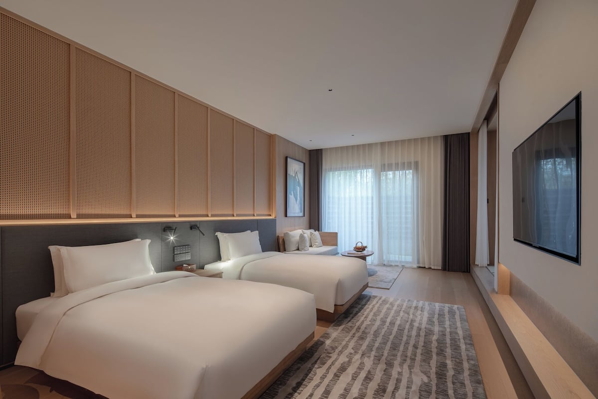Quarto de hotel moderno com duas camas, uma TV grande e vista para o exterior.