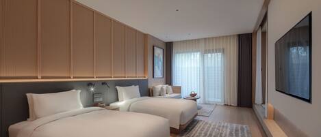 A modern hotel room with two beds, a large TV, and a view of the outdoors.