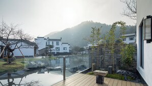 A serene outdoor deck with a glass railing overlooking a calm water feature and a traditional building in the background. - Huangshan Misty Rain Resort Hotel (Huangshan)