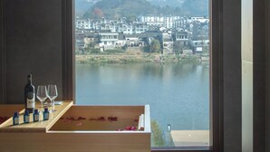 A modern room with a large window overlooking a river and a town. - Huangshan Misty Rain Resort Hotel (Huangshan)