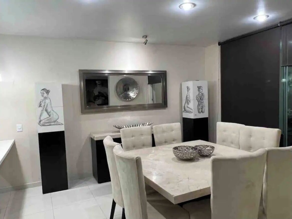Un espace repas moderne avec une table en marbre, des chaises à revêtement blanc et des œuvres d’art décoratives sur les murs.