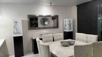 Un espace repas moderne avec une table en marbre, des chaises à revêtement blanc et des œuvres d’art décoratives sur les murs.
