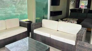 A modern living room with wicker sofas, a glass coffee table, and a flat-screen TV mounted on the wall. - Leon House (Jardines de la Calera)