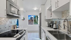 A modern kitchen with stainless steel appliances, white cabinetry, and a view of the city through a window. - 2BR Designer Condo, Free Parking, Convention Ctr (Seattle)