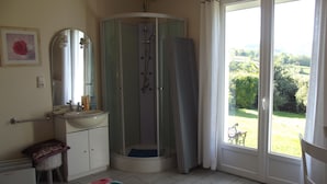Un baño con ducha, lavamanos, espejo y ventana con vistas a un jardín.