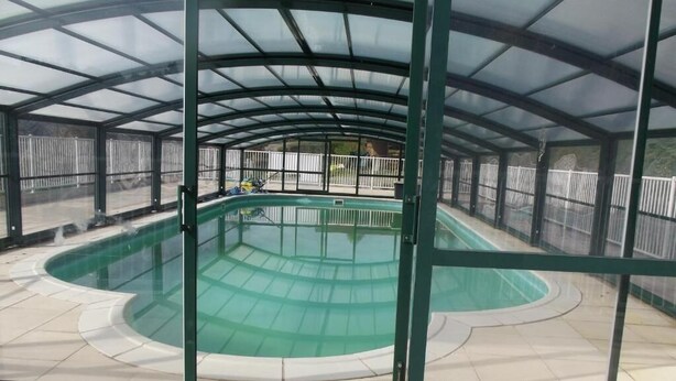 Una piscina techada con cerramiento de vidrio, suelo de baldosas y estructura de metal.