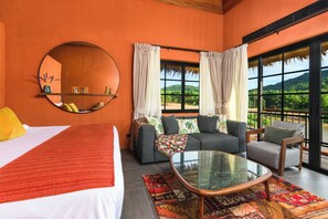 Une chambre d’hôtel avec un lit, un canapé, une table basse en verre et une grande fenêtre avec des rideaux.