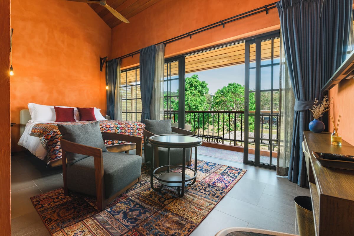 A bedroom with a bed, a chair, a small table, and a view of the outdoors through large windows.