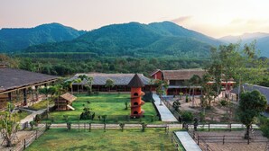 A traditional building with a thatched roof, surrounded by a well-maintained lawn and a fenced area. - Niran Farm (Si Sunthon)