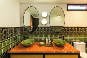 Une salle de bain avec deux vasques vertes posées sur un comptoir en marbre, un miroir et un mur recouvert de carreaux.