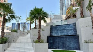 A modern building with a staircase leading to a dark blue wall, surrounded by palm trees and a well-maintained lawn.