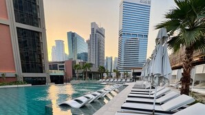 A swimming pool with lounge chairs and umbrellas, surrounded by high-rise buildings.