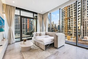 A modern living room with a sofa, a coffee table, and a view of a cityscape with buildings and construction cranes.