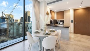 A modern dining area with a table set for four, a kitchen with dark cabinetry, and a view of a cityscape with construction cranes.