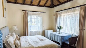 Ein Schlafzimmer mit Bett, Schreibtisch, Stuhl, Lampe und einem Fenster mit Vorhängen.