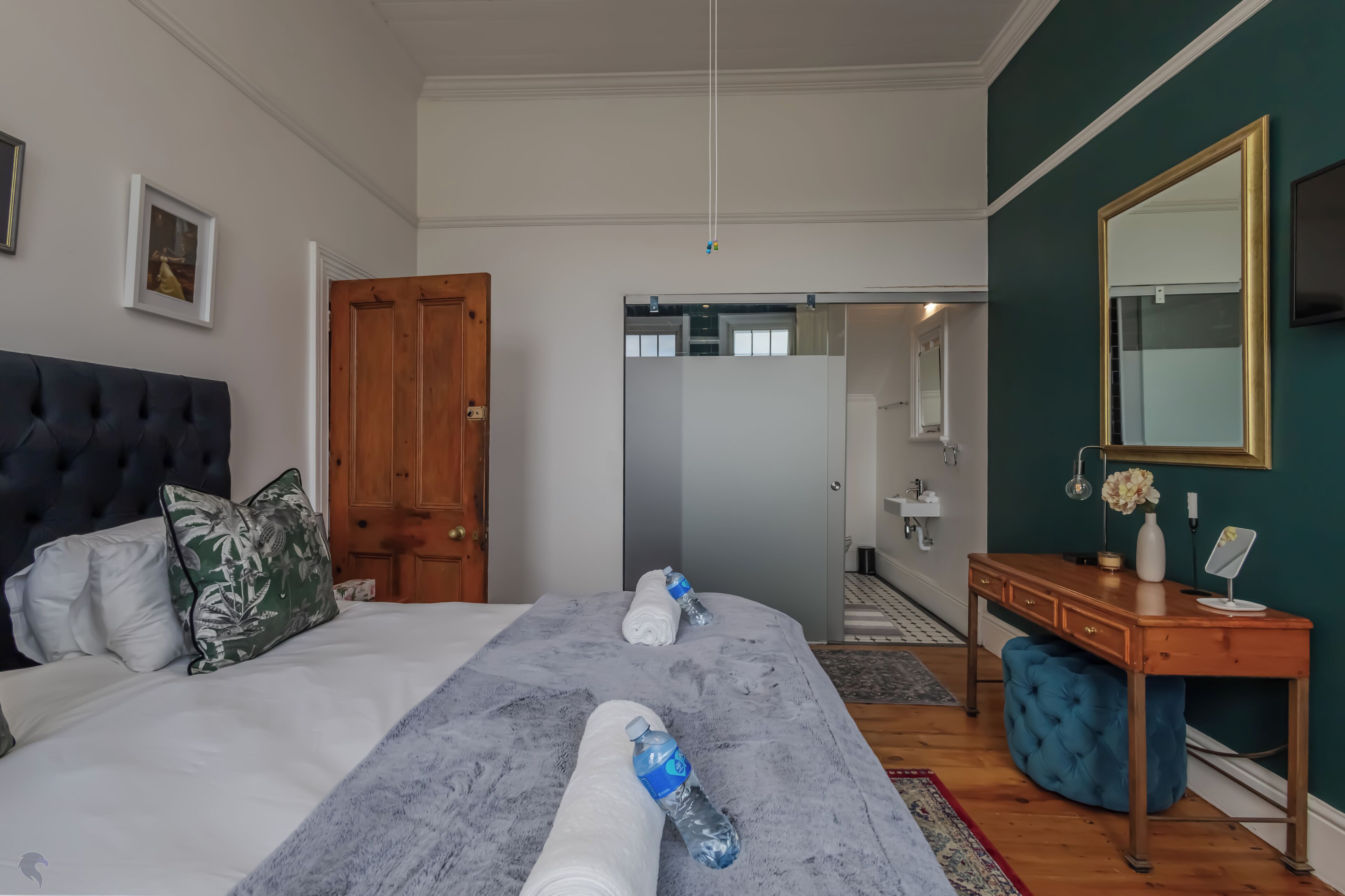 Une chambre à coucher avec un lit, un bureau en bois, un miroir et une porte.
