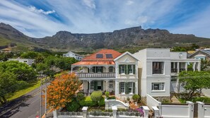 A two-story house with a red roof, white walls, and a balcony. It is located in a residential area with mountains in the background. - Belvedere House (Cape Town)